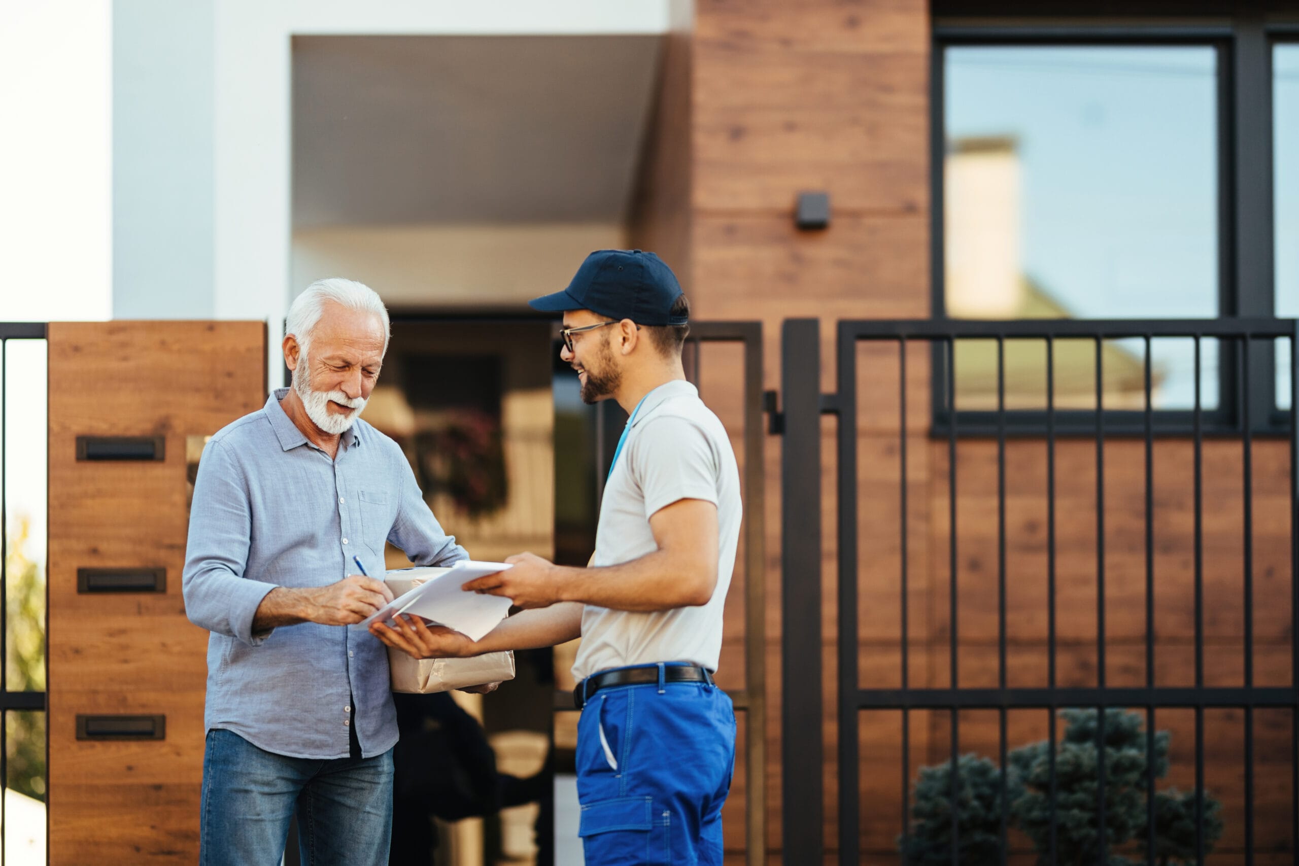 happy mature man receiving package from courier signing paperwork front his house scaled