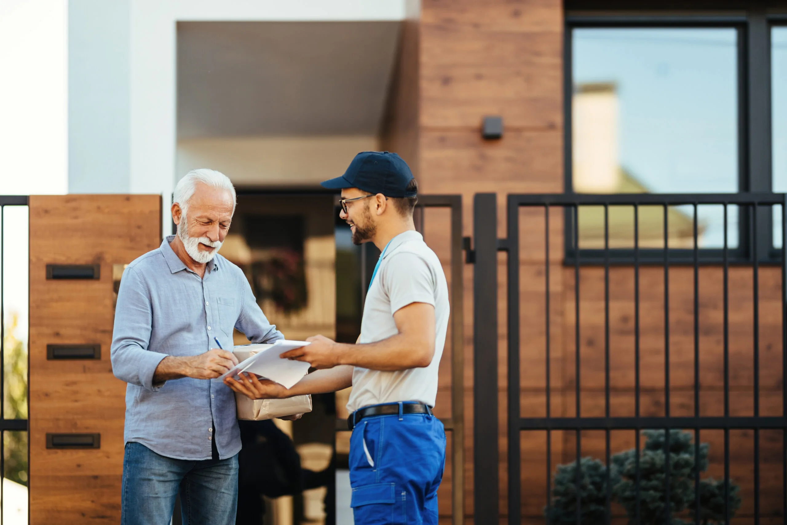 happy mature man receiving package from courier signing paperwork front his house scaled